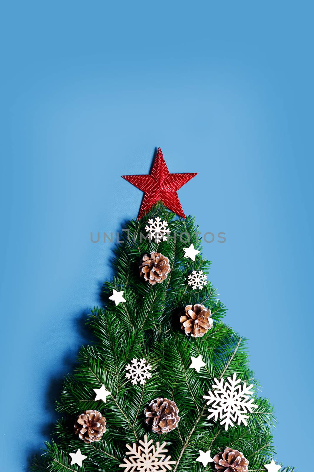 Christmas tree made of natural spruce branches deecor with red star on blue background, flat lay card with copy space