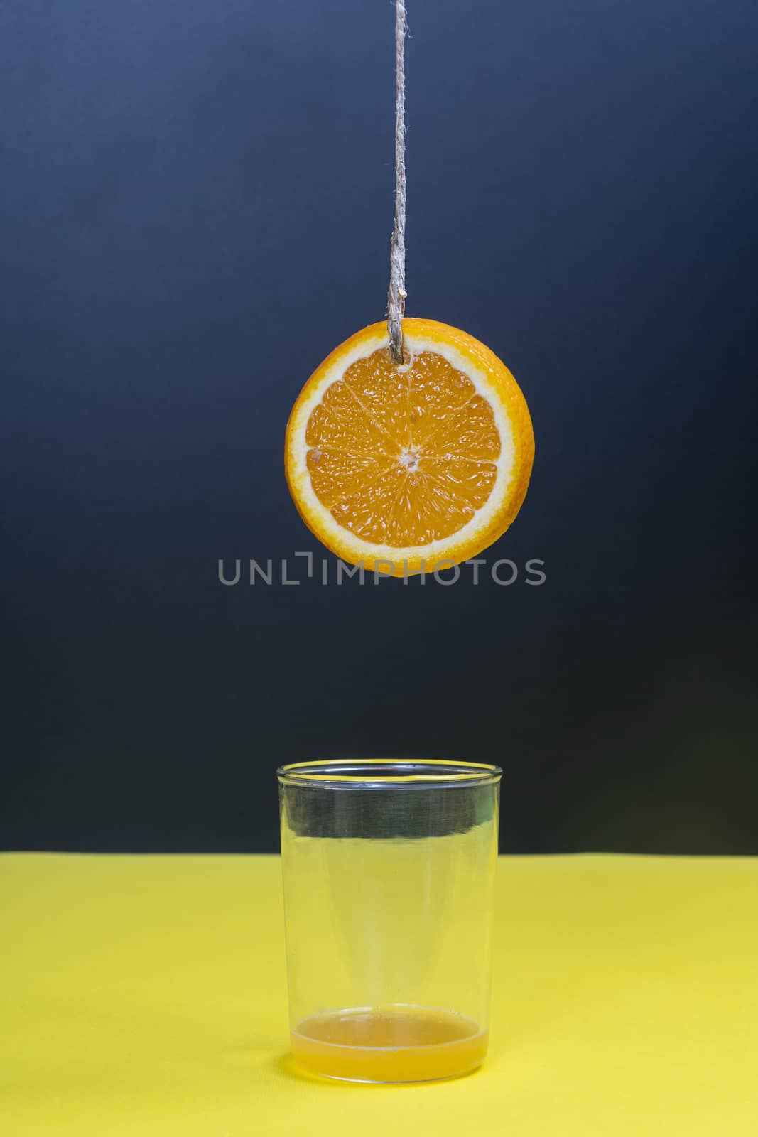 a slice of orange hanging by a thread over a glass