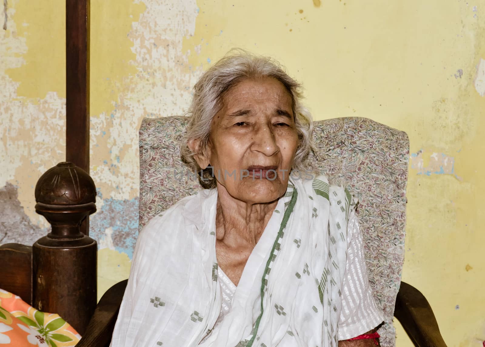 Portrait of smiling Active senior Asian and Indian Ethnicity woman of 82 years sitting on chair resting at home while looking at camera.