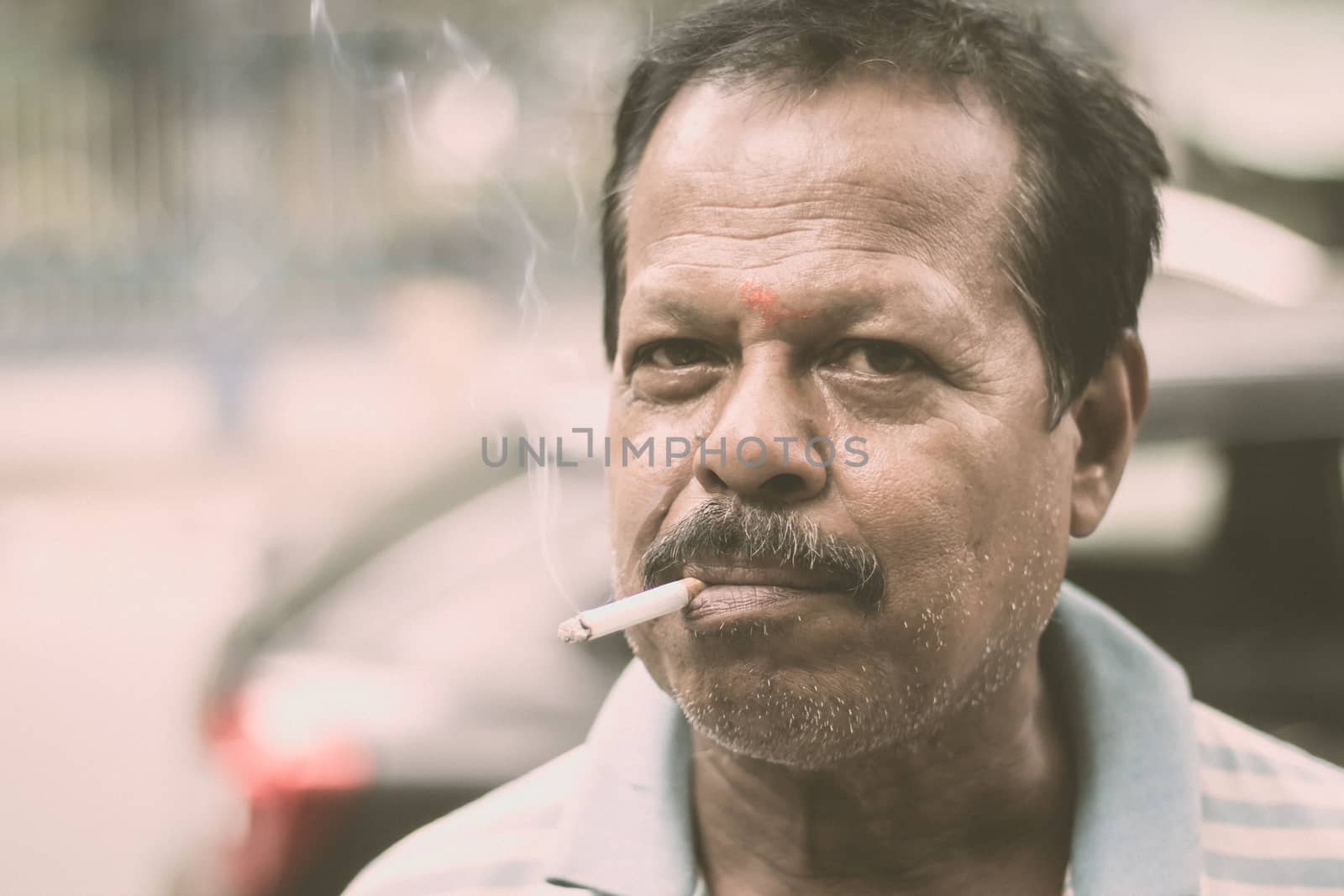 Portrait of a A mid adult senior mature man of Asian and Indian Ethnicity is smoking cigarette. Front View. Close up. Photography taken on 31 May 2019 on World No Tobacco or anti Tobacco Day, in a city street of India, South Asia. by sudiptabhowmick