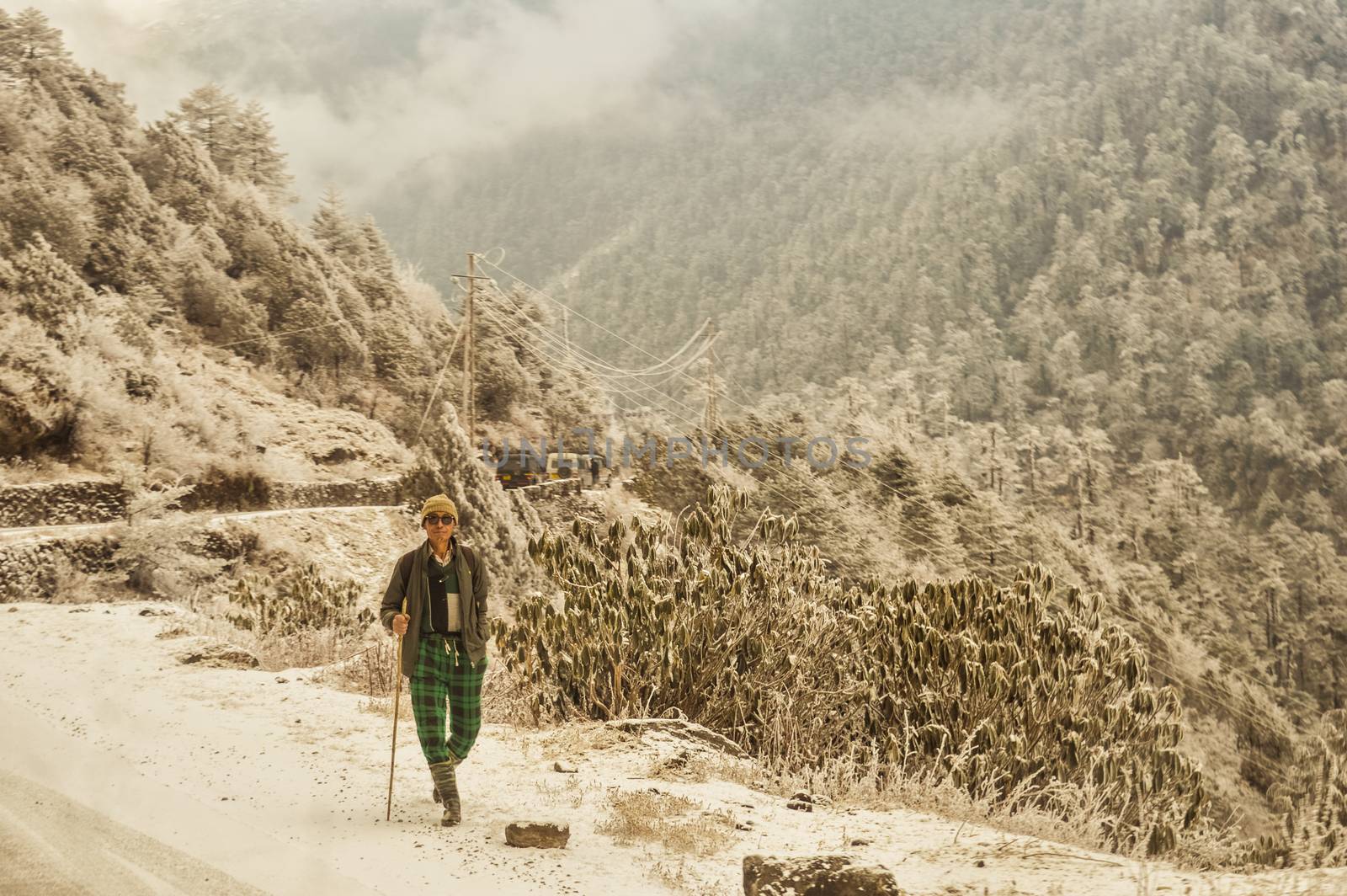 A Mature old (a man of Nepalese ethnicity) solitary hiker on a hiking trail walking alone in a beautiful winter environment of North east Himalayan Mountain range. Nepal, South Asia.