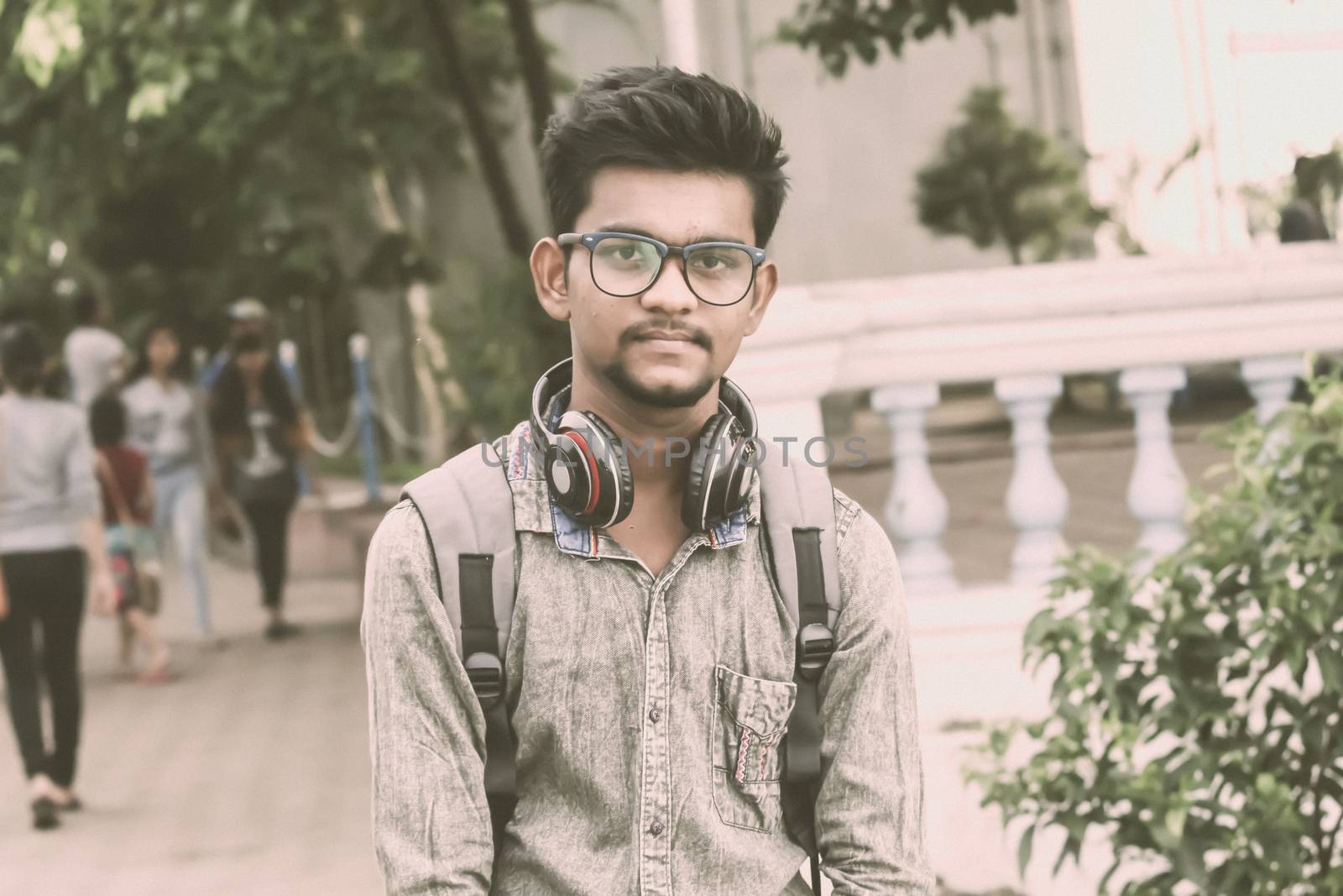 Half length portrait of attractive young a man called Ahok standing outdoors with modern headphones and looking at camera. A music student portrait photography on 21 June, World Music Day. by sudiptabhowmick