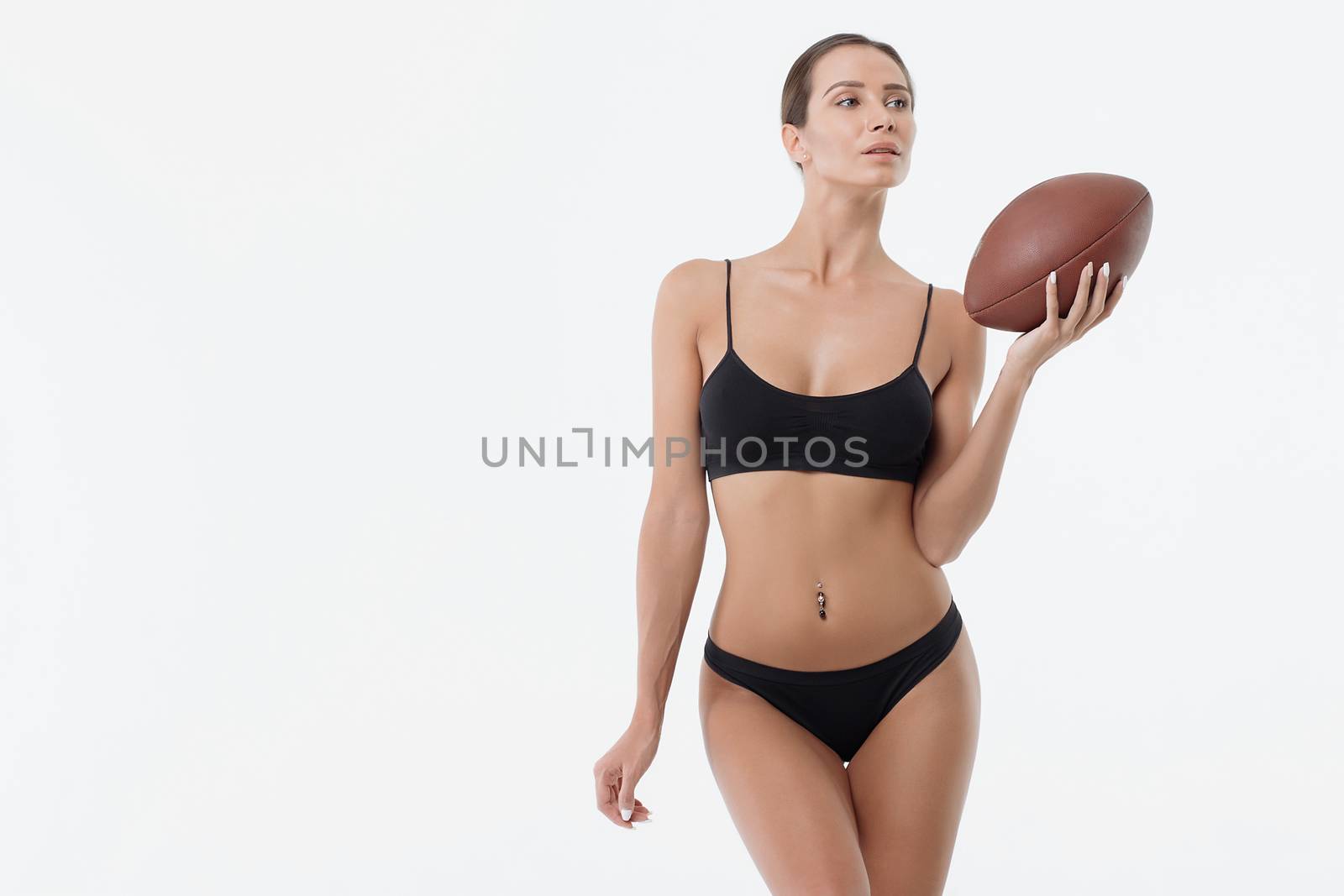 Attractive erotic young woman in lingerie holding rugby ball and looking at camera