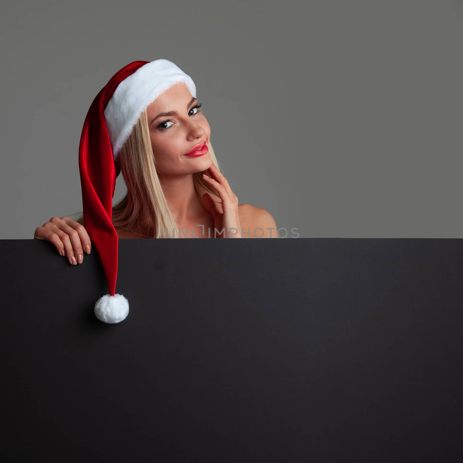 Santa girl holding blank black sign billboard. Christmas woman in Santa hat showing paper sign.