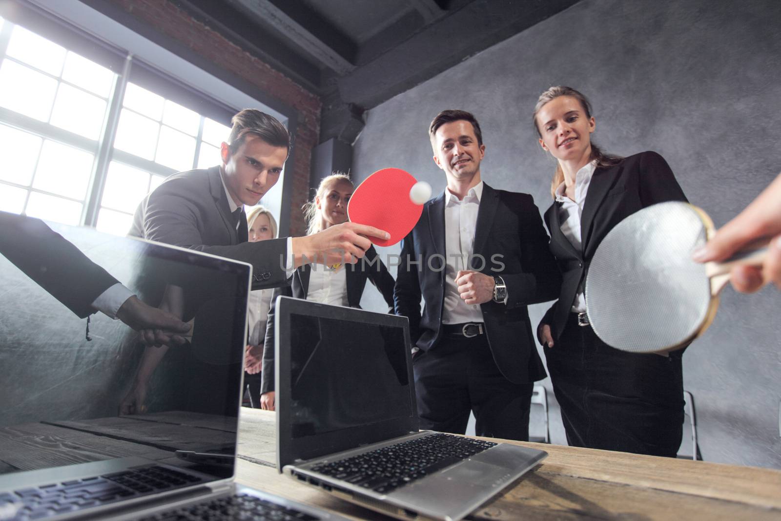 Business people play ping pong on office table with laptops