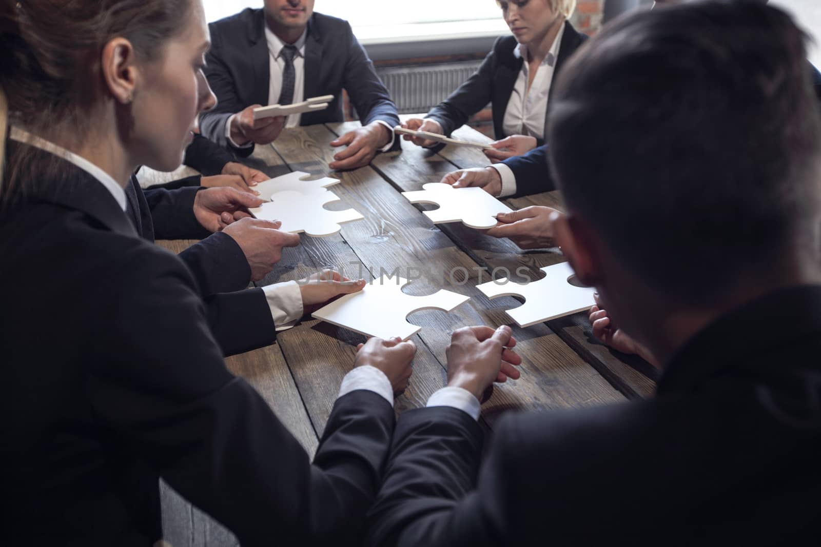 Business people and puzzle on wooden table, teamwork concept