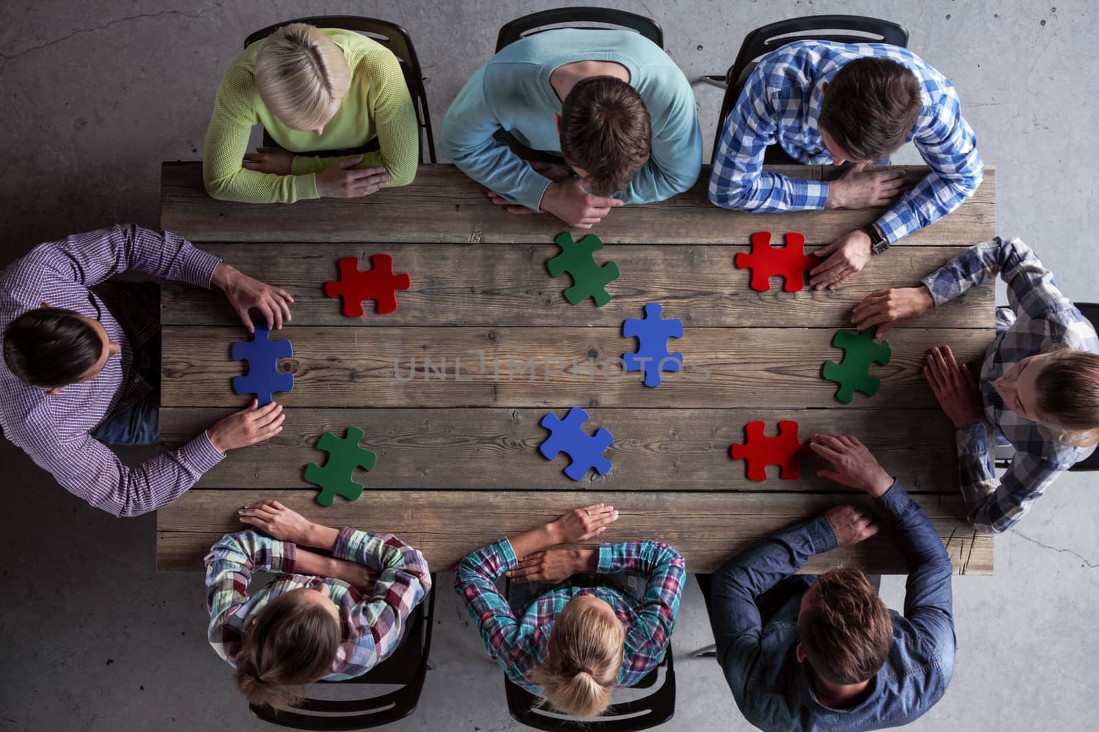 Business people and puzzle on wooden table, teamwork concept