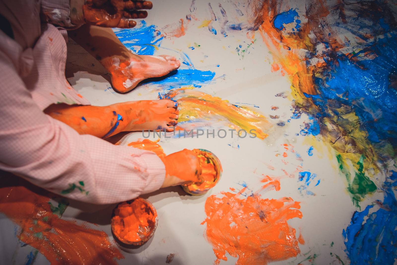 Kid painting a big paper with hos or her hands and barefoot in multiple colors
