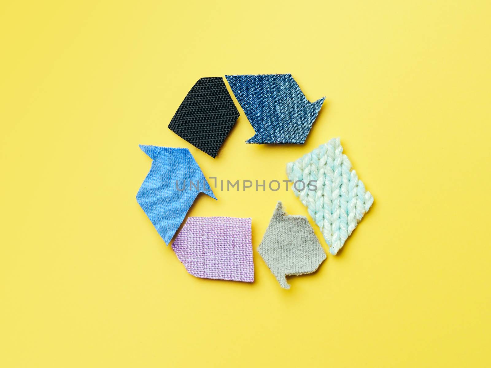Reuse, reduce, recycle concept background. Recycle symbol made from old clothing on yellow background. Top view or flat lay.