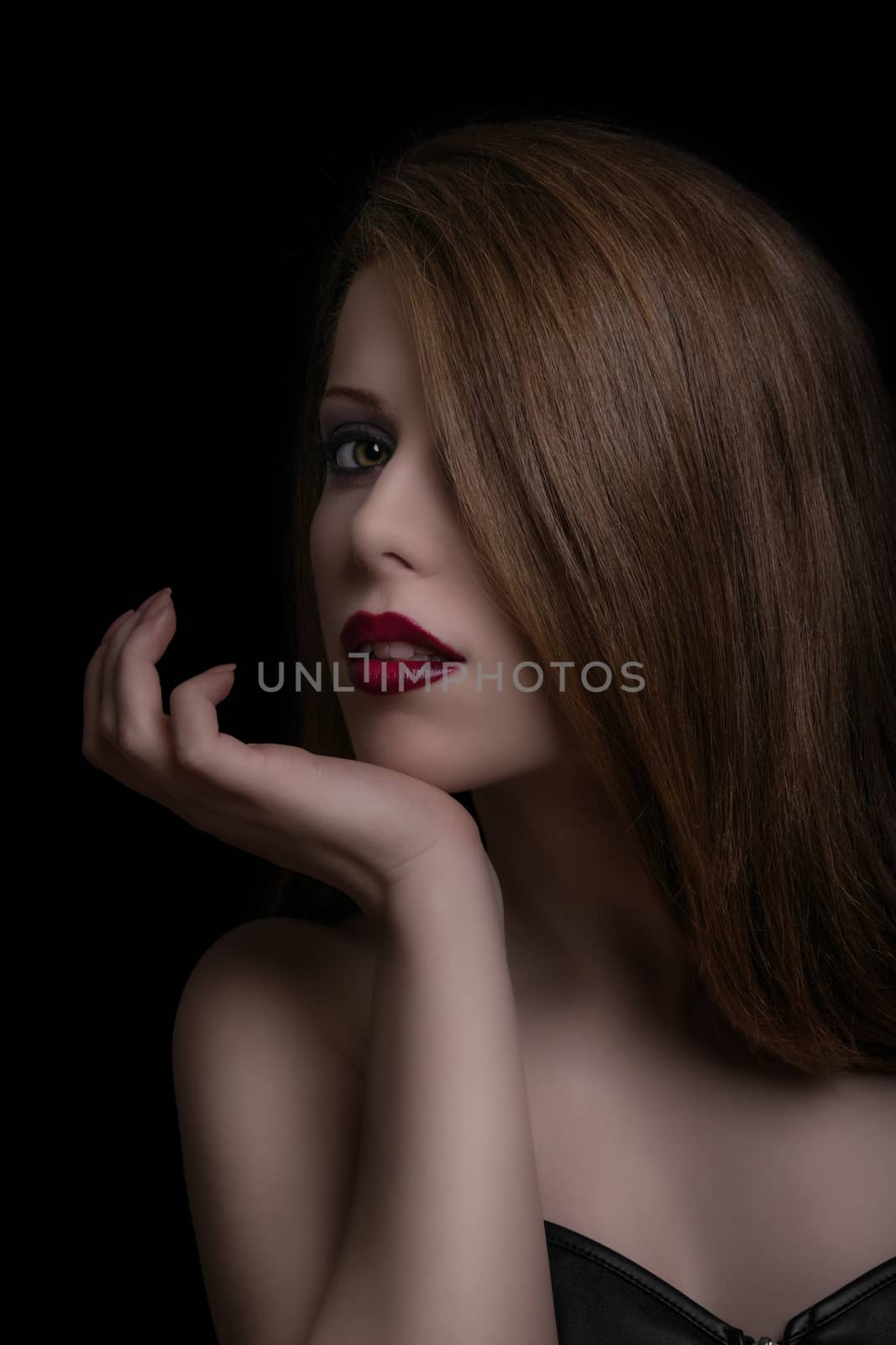 Low key sensual, make up and beauty portrait of a young woman with red lipstick on black background.
