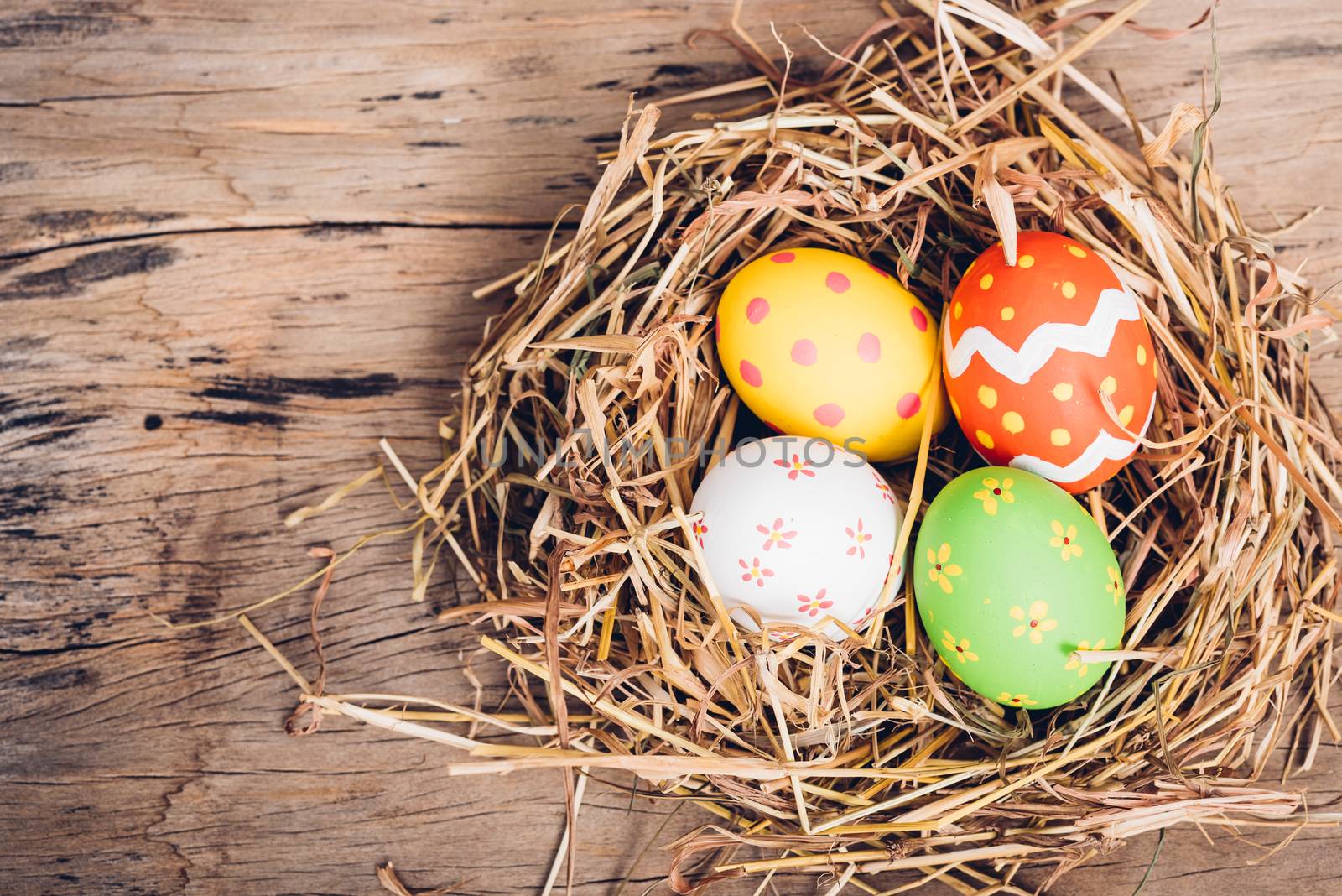 Beautiful Easter multi color egg in straw on wooden background, Easter day concept