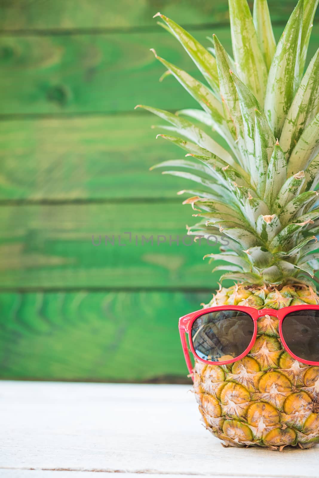 Holiday pineapple have sunglasses on green wooden background, tropical holiday concept