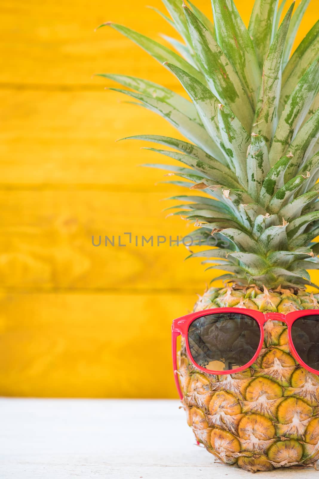 Holiday pineapple have sunglasses on yellow wooden background, tropical holiday concept