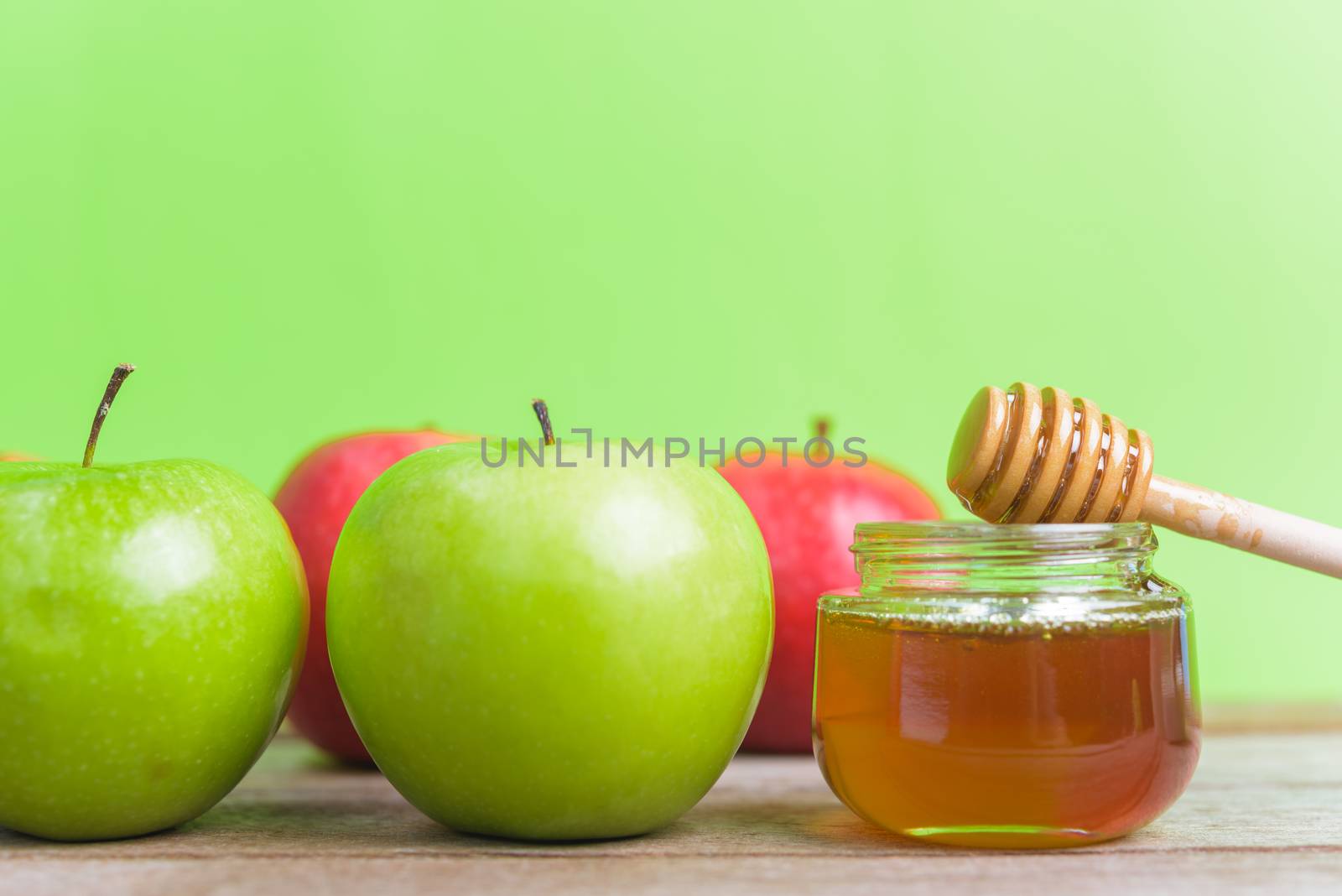 Jewish holiday, Apple Rosh Hashanah dessert, on the photo have honey in jar have red apples and green apples on wooden with green background