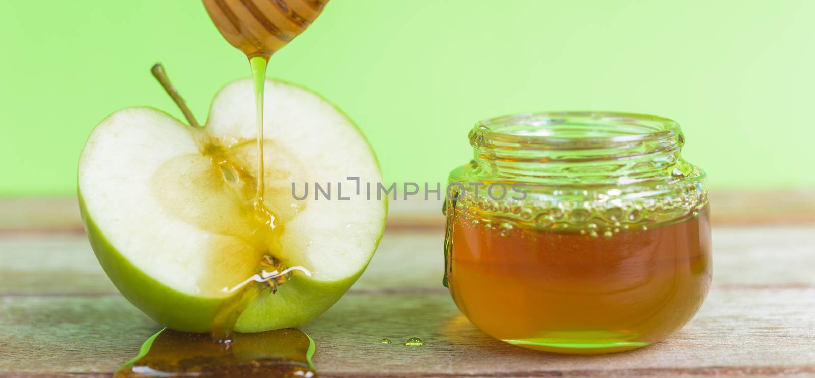 Jewish holiday, Apple Rosh Hashanah, on the photo have honey in jar and drop honey on green apples on wooden with green background