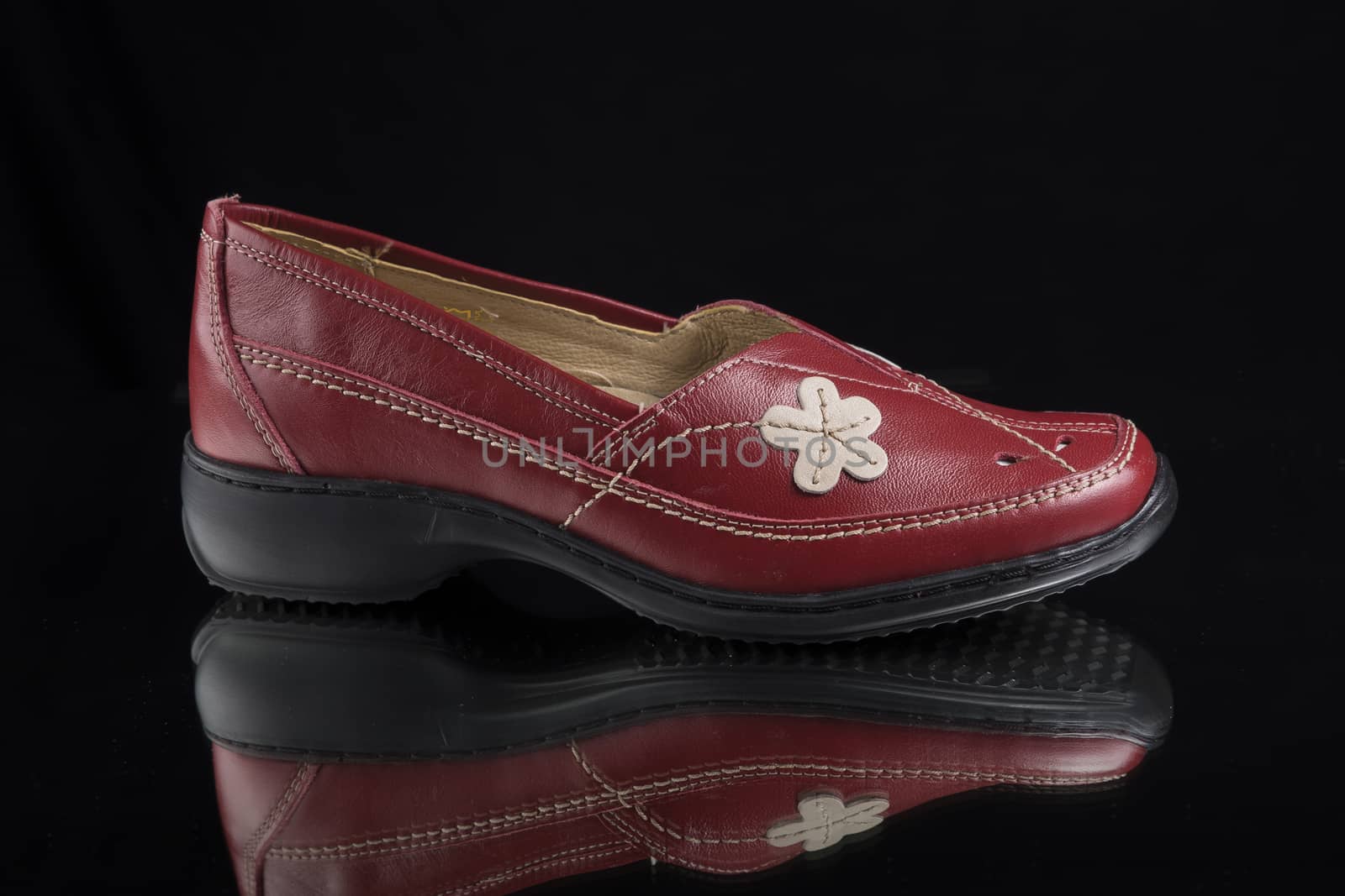 Female red leather shoe on black background, isolated product.