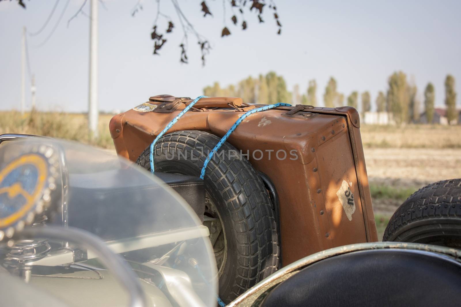 Old vintage leather suitcase, attached to an old vintage vehicle Italian ready to go and venture into a new journey. Abientazione: Italian countryside.