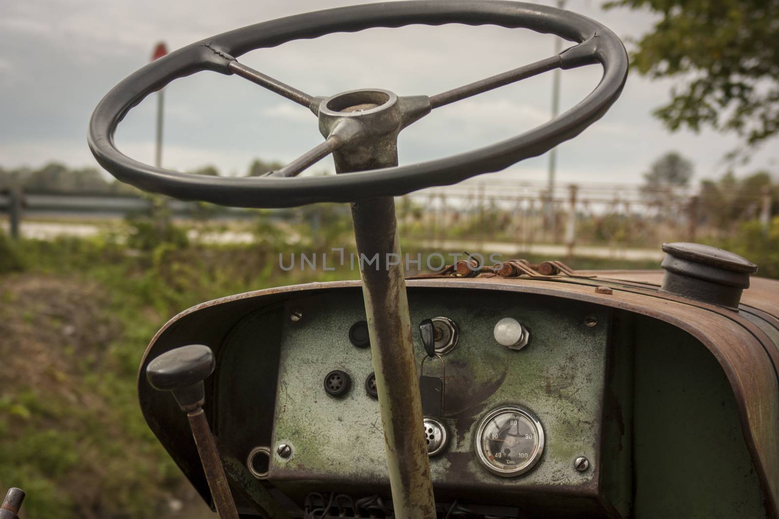 Details of the steering wheel and instrumentation of an old farm tractor nestled in the countryside during a work day.