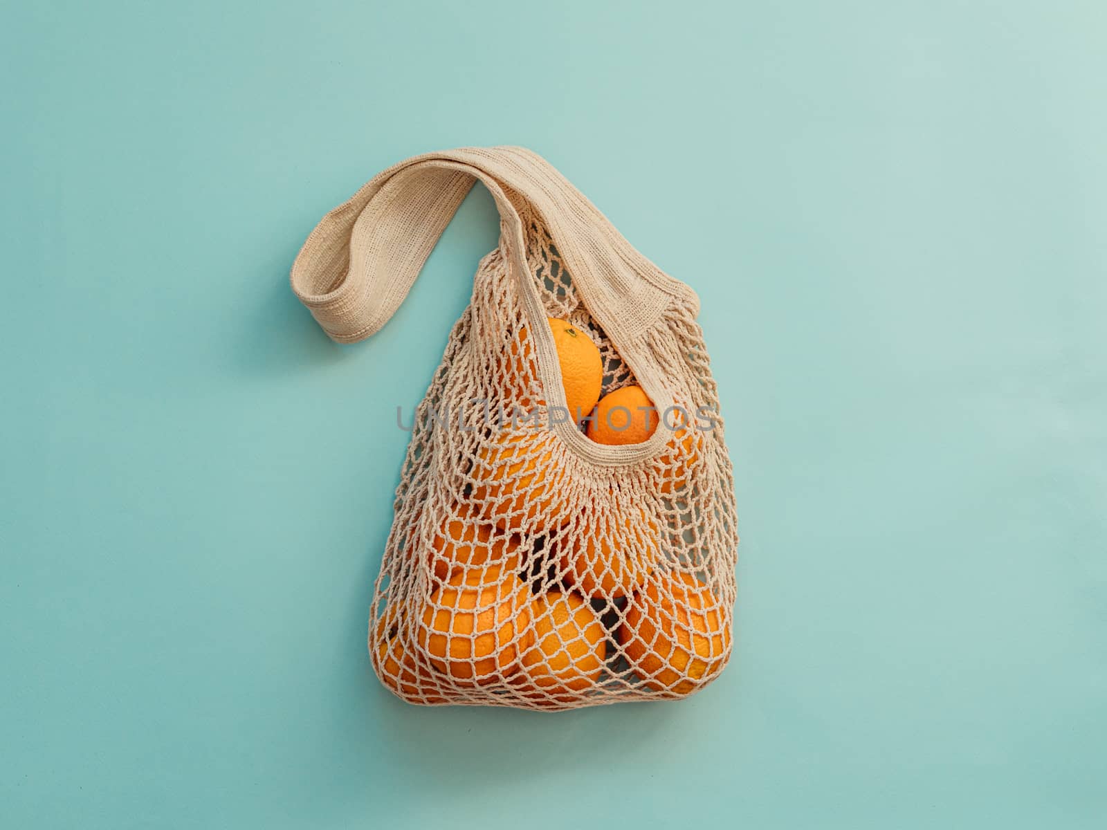 Mesh bag with fruits on blue background. Modern reusable shopping and zero waste concept.