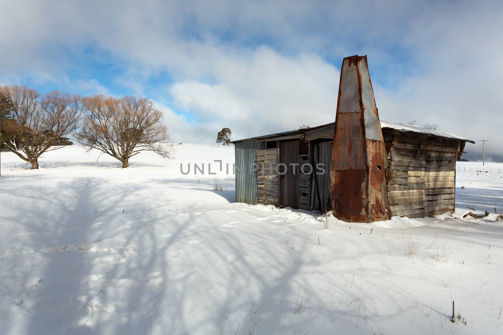 Old timber shack, shed or stable in a rural paddock with full coverage snowfall in winter. Blue sky makes a brief appearance between snow fluries