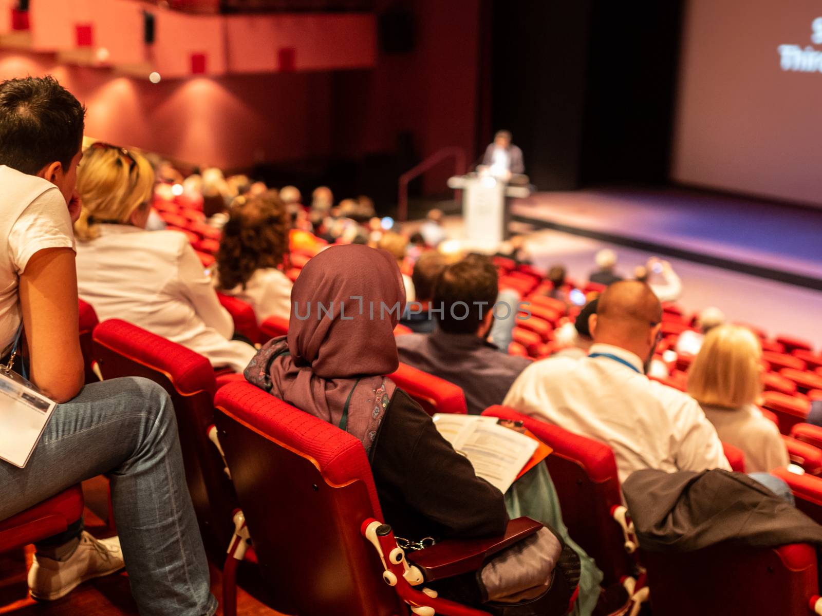 Speaker giving a talk in conference hall at business event. Audience at the conference hall. Business and Entrepreneurship concept. Focus on unrecognizable people in audience.