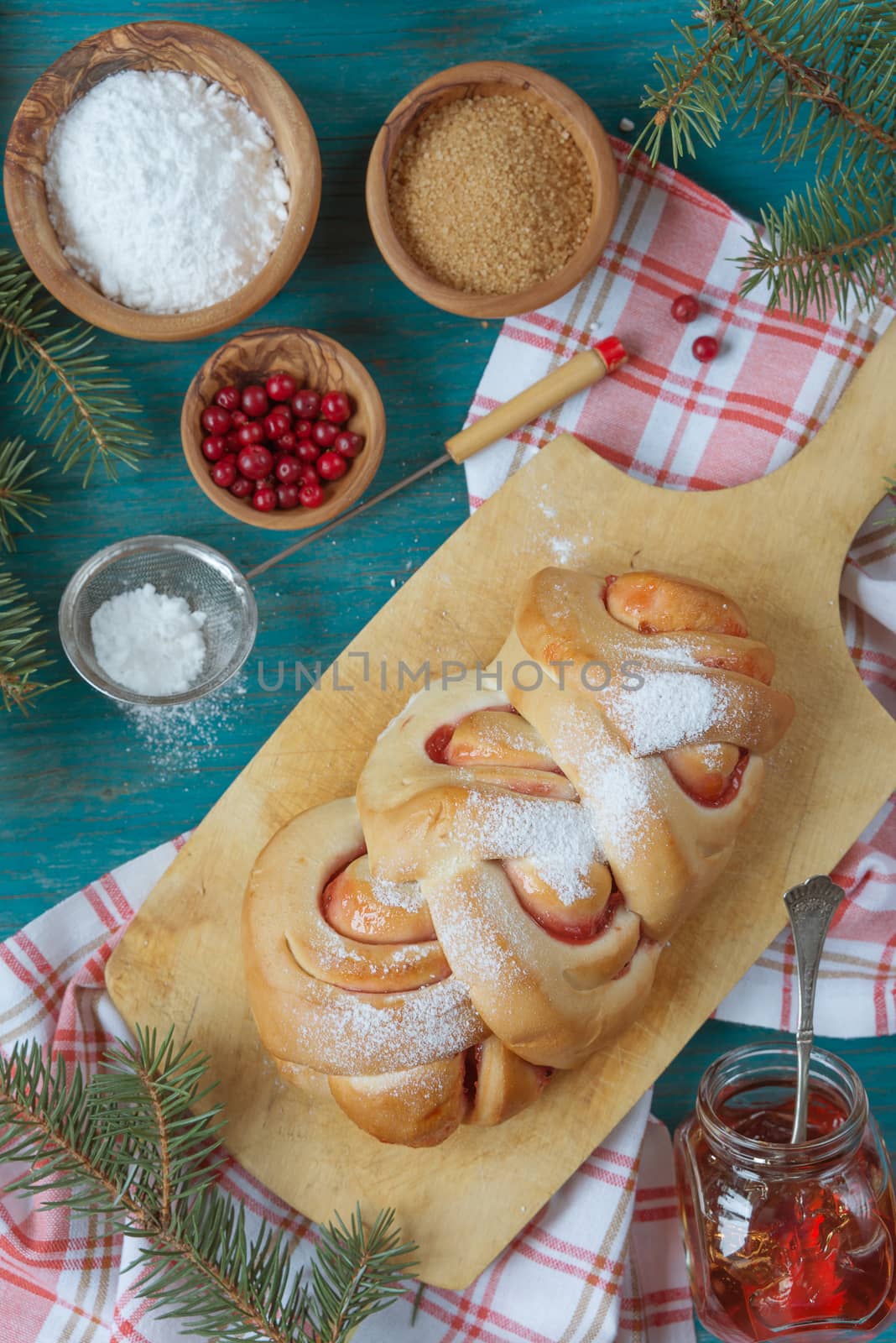 Sweet Christmas pastries with a cowberry jam on an old cutting board surrounded by fir branches, top view