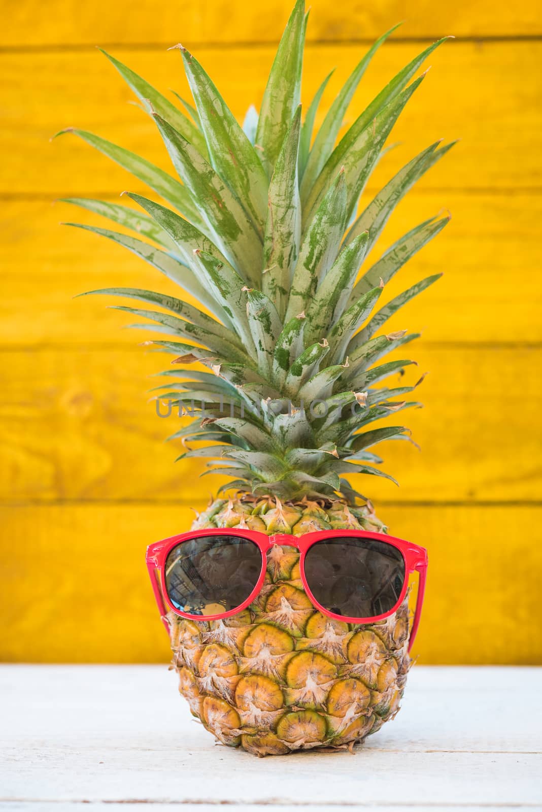 Holiday pineapple have sunglasses on yellow wooden background, tropical holiday concept