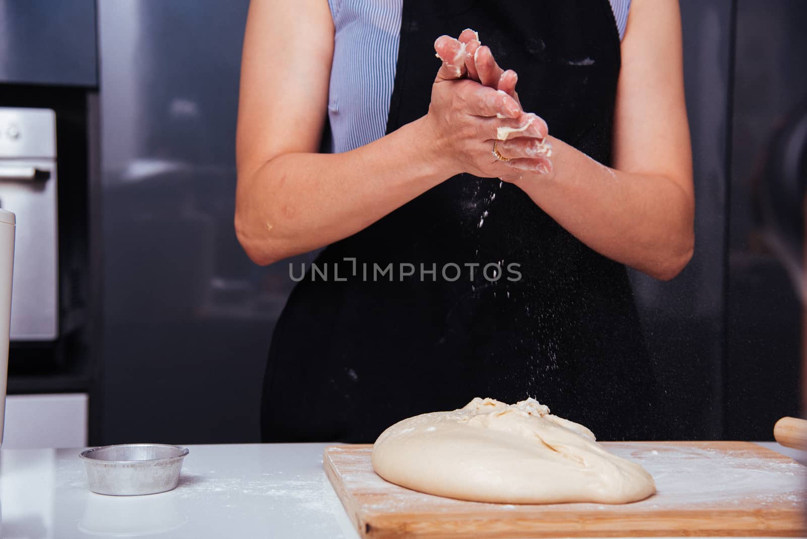 Hands of baker woman female making sprinkling clapping flour dough on table