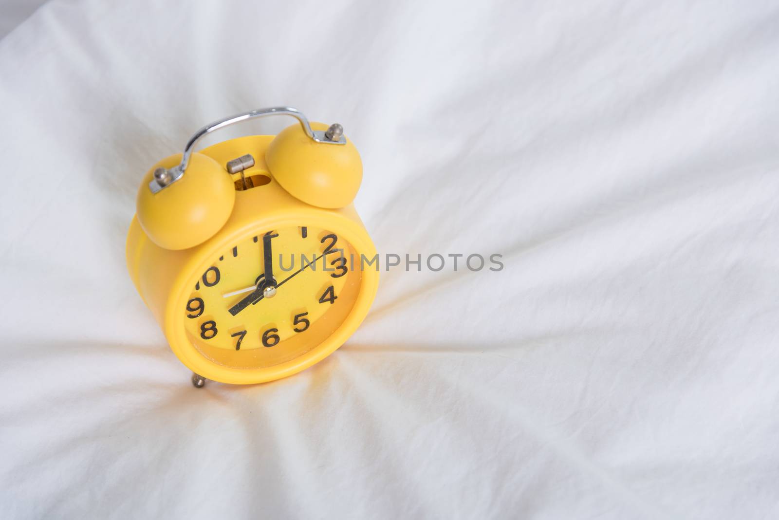 Yellow Alarm clock at 8 am on the bed. to wake up
