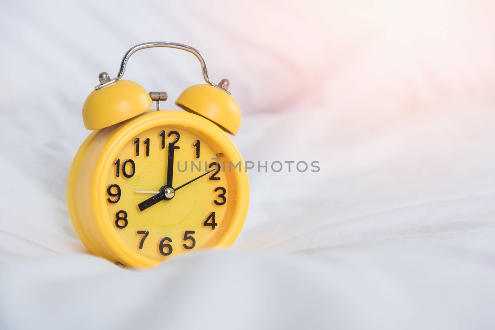 Yellow Alarm clock at 8 am on the bed. to wake up