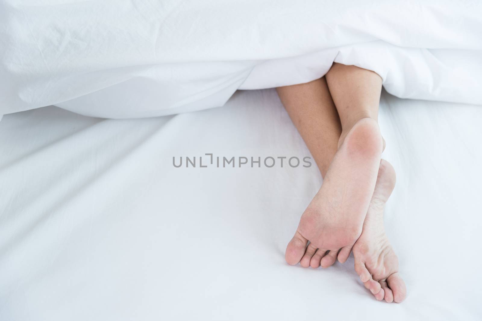 Under white blanket covers with feet showing by Sorapop