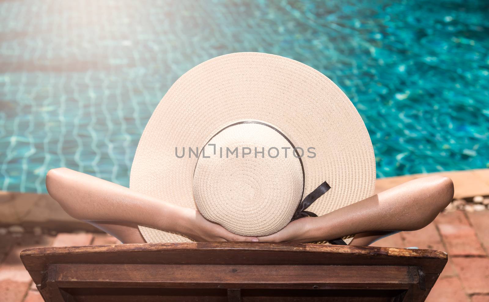 Asian young  woman in big hat taking sunbath at swimming pool poolside blue water