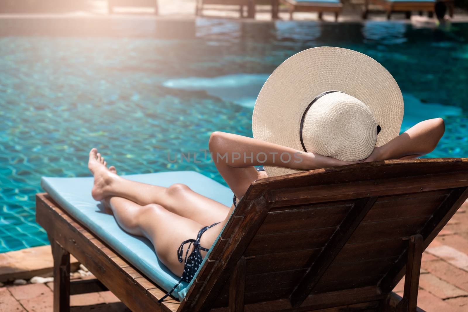 Asian young  woman in big hat taking sunbath at swimming pool poolside blue water