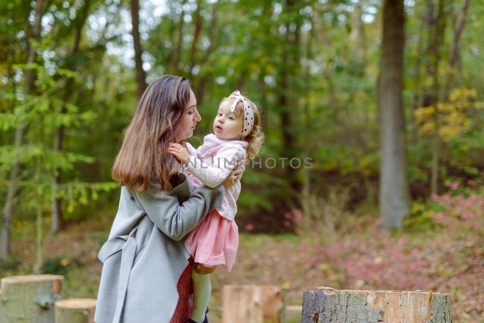 Mother holds daughter in her arms in the park on a sunny day. Autumn day