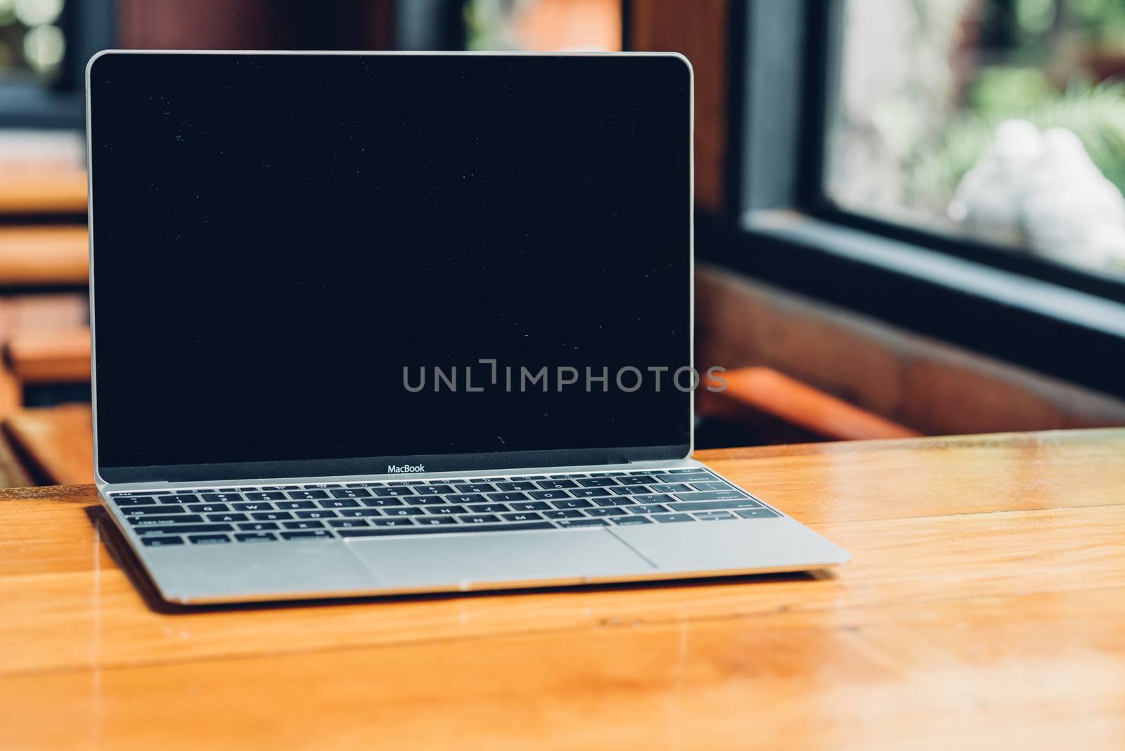 Laptop computer mockup with blank screen on desk in coffee shop.