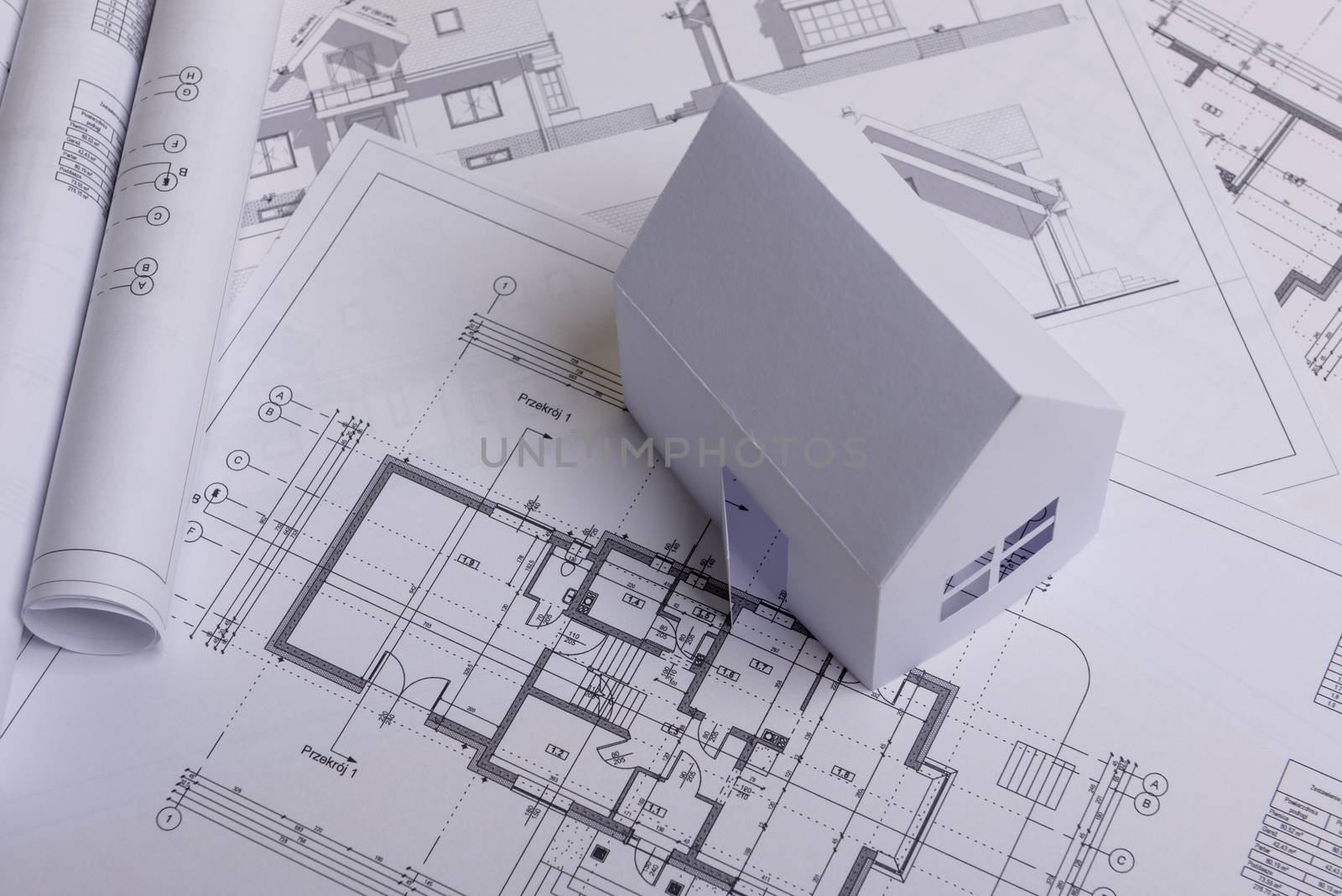 White family paper house, house projects plan and blueprints in the background. Minimalistic and simple concept, style. Horizontal orientation