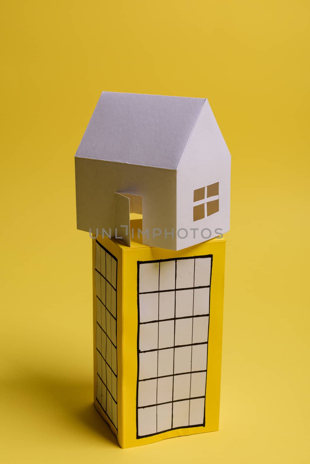 White family paper house over block of flats on yellow background paper. Minimalistic and simple concept, style. Copy space. Vertical orientation.
