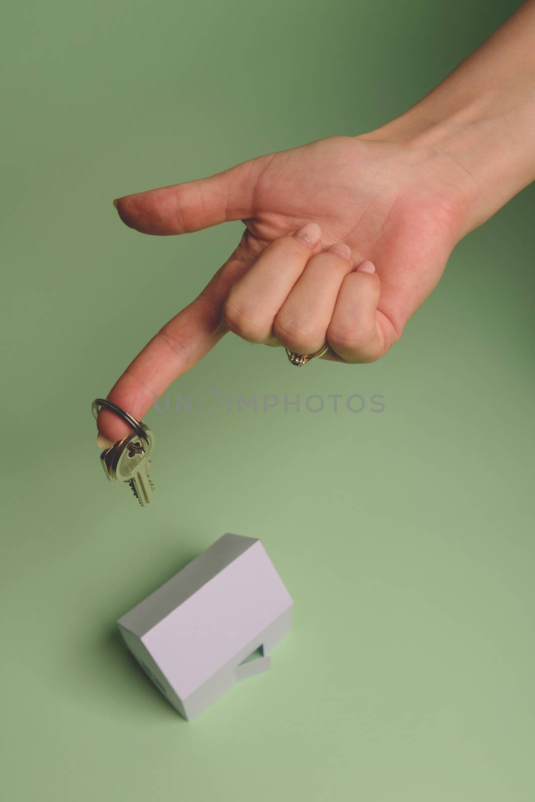 White family paper house. House keys in hand on mint background paper. Minimalistic and simple concept, style. Copy space. Vertical orientation. Family moving or removal concept.