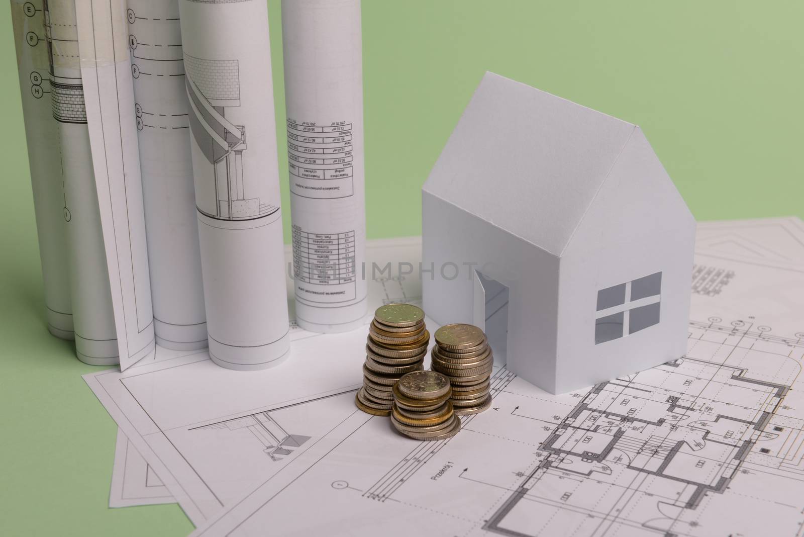 White family paper house , stack of money coins, house projects plan and blueprints on mint background paper. Minimalistic and simple concept, style. Horizontal orientation