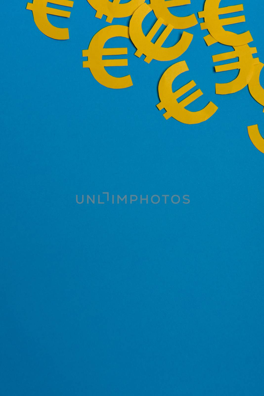 Paper yellow symbols of euro currency on blue background. View from above with copy space