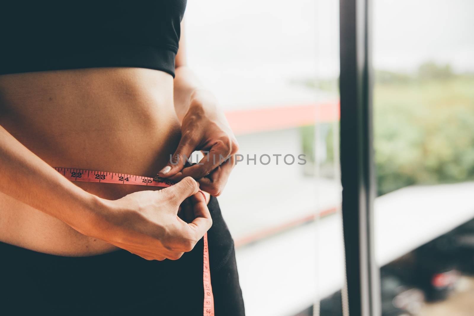 Beautiful woman using tape measuring waist, her is body slim after workout at fitness GYM
