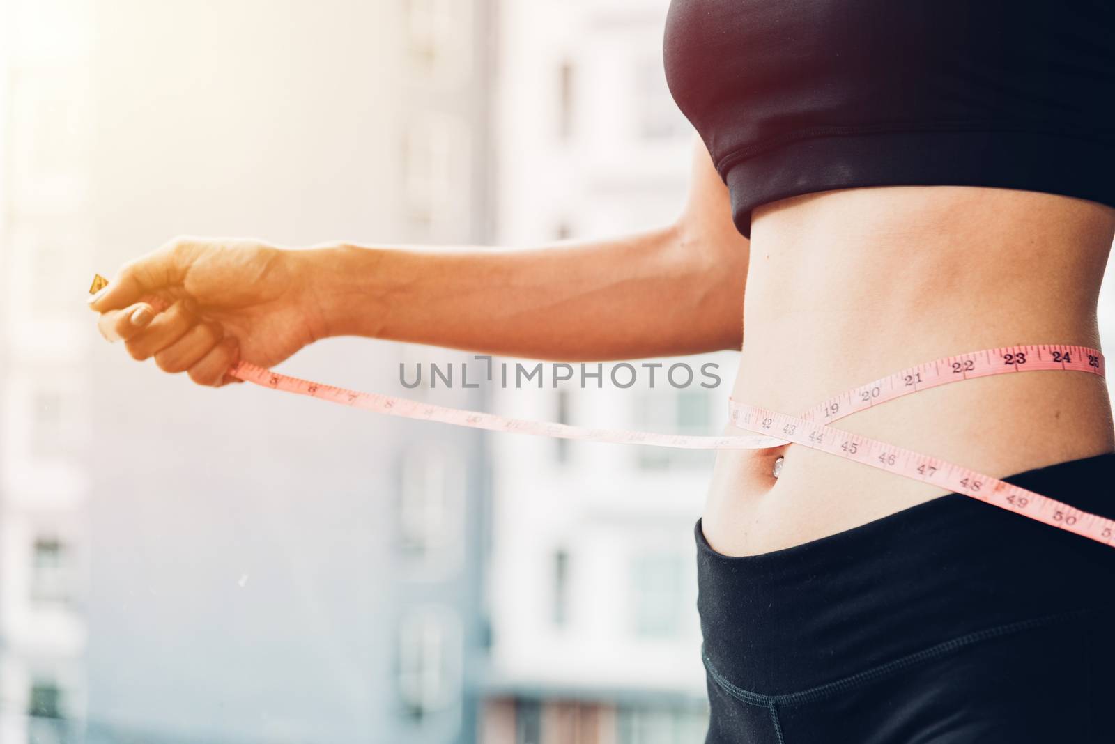 Beautiful woman using tape measuring waist, her is body slim after workout at fitness GYM