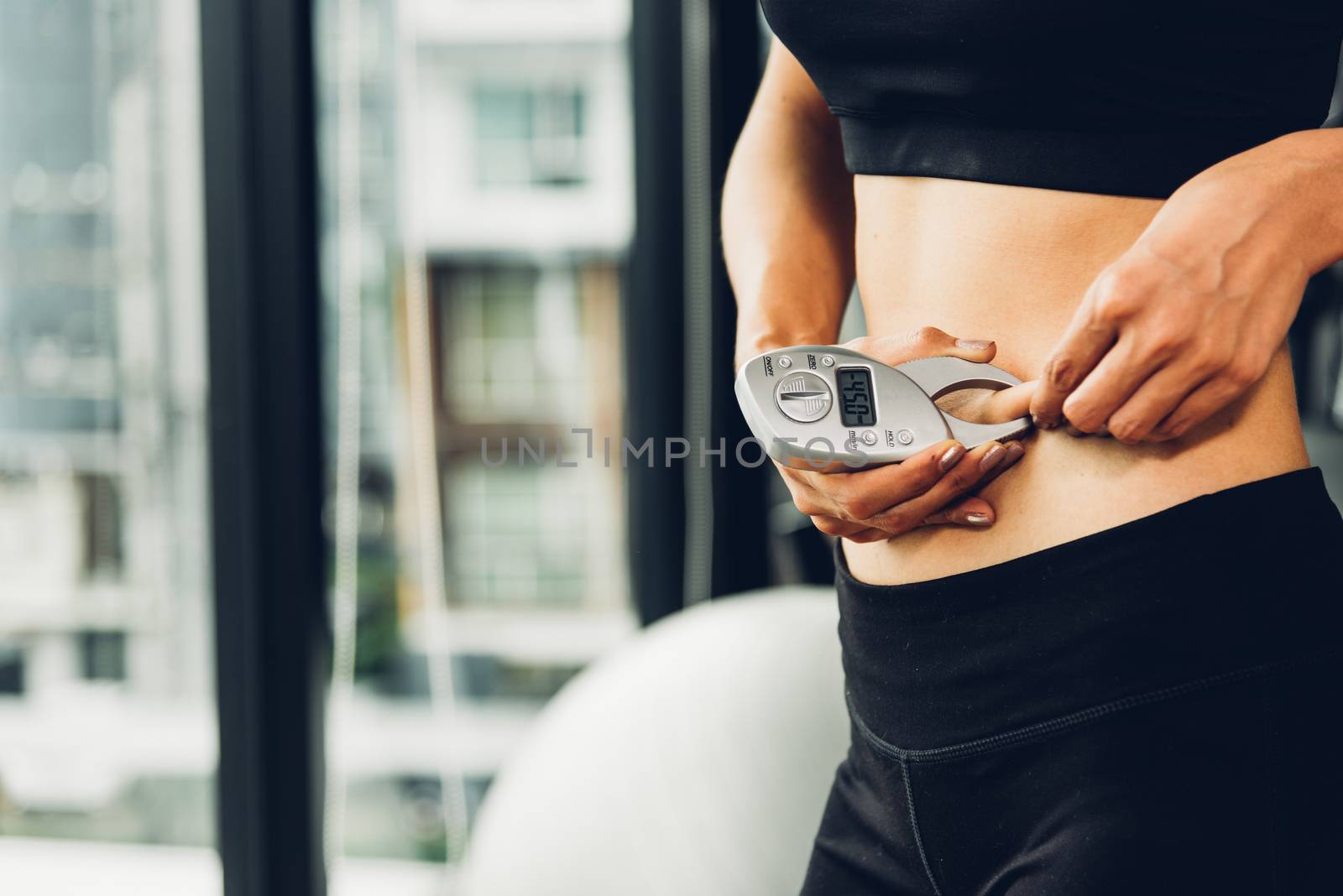 Beautiful woman using caliper fat measure after exercise workout out at fitness GYM