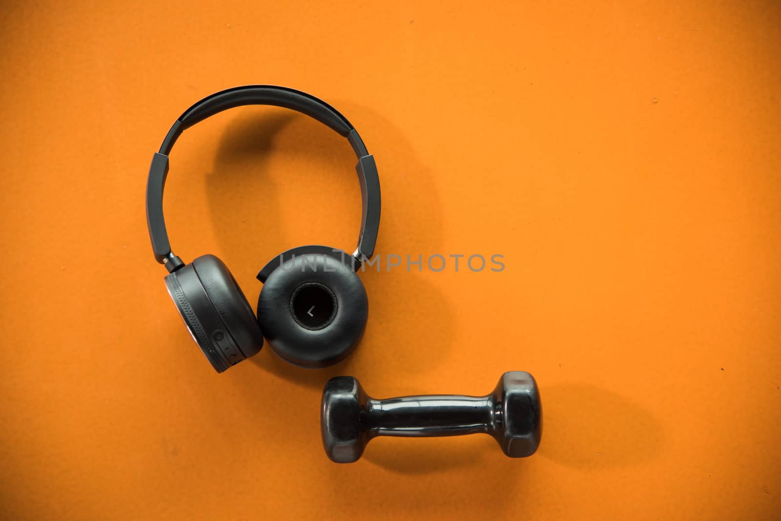 Music headphones and dumbbell on orange rubber floor in fitness gym