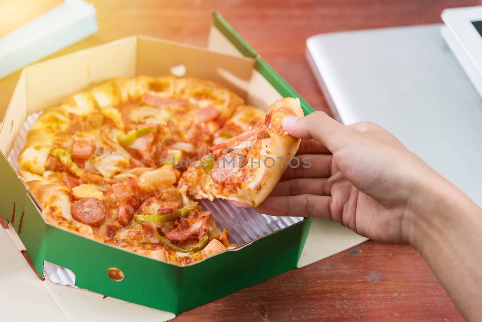 Hands taking pizza slices from green box