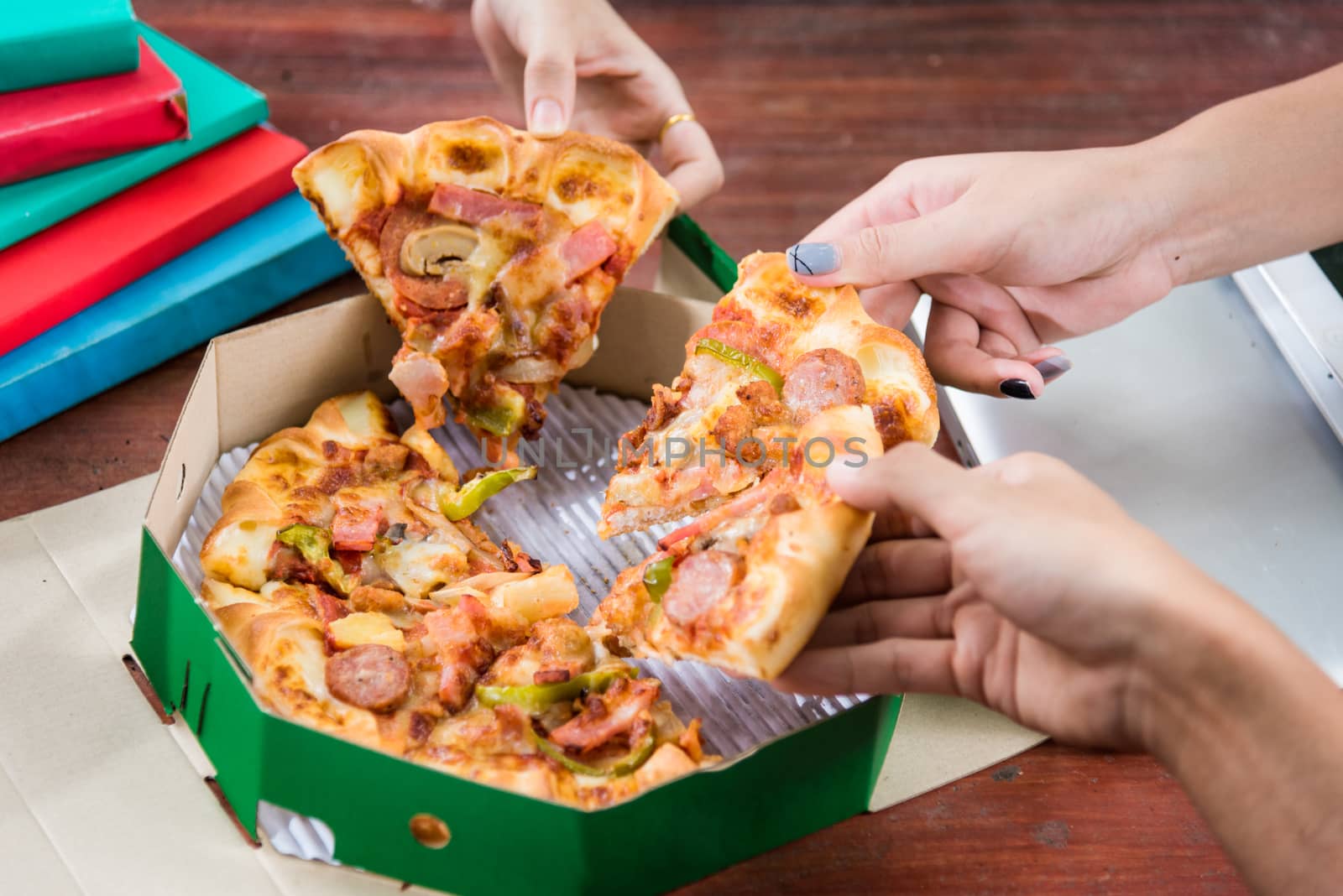 Hands taking pizza slices from green box