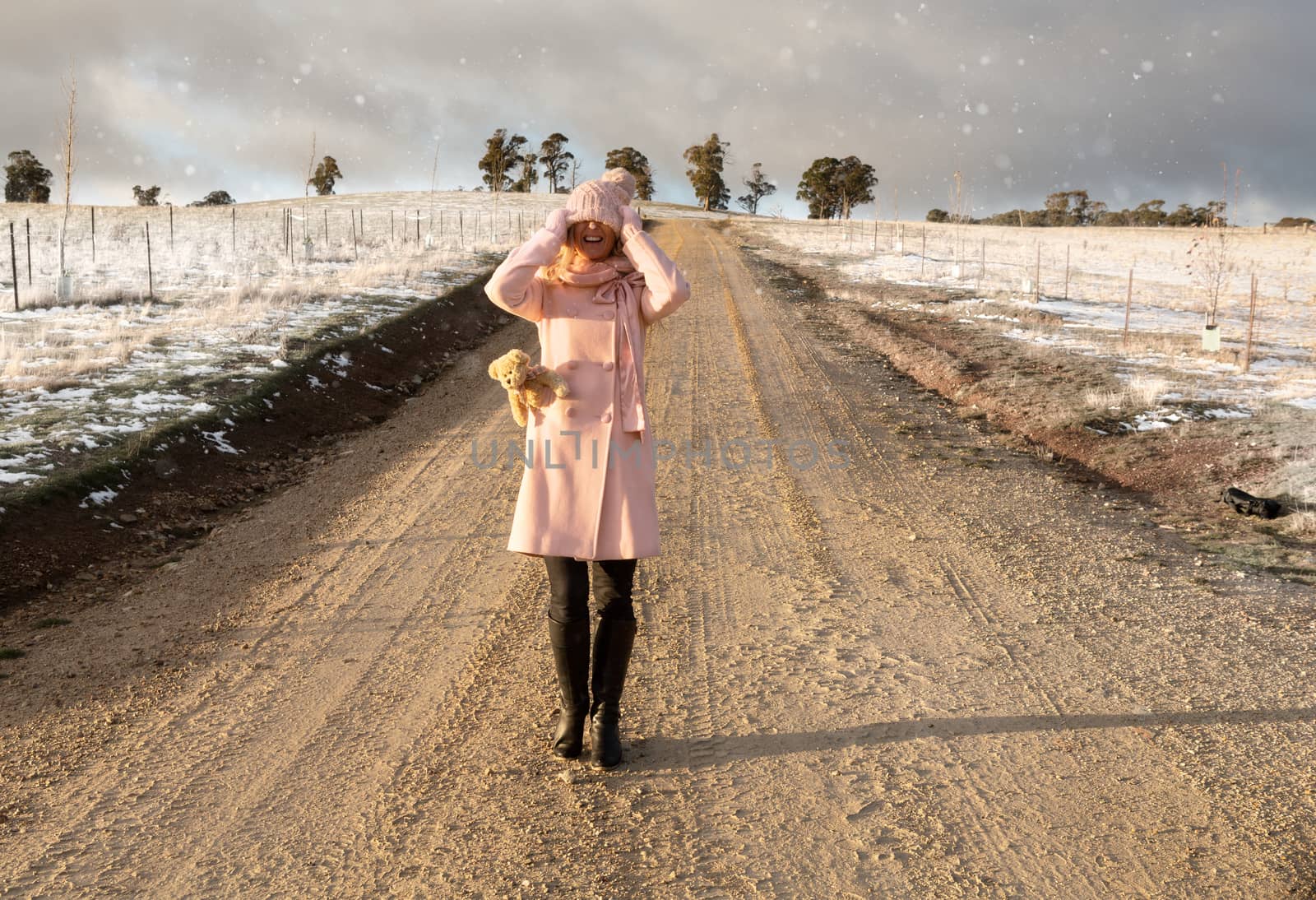 Happy go lucky woman walking down dirt road in light snow fall by lovleah