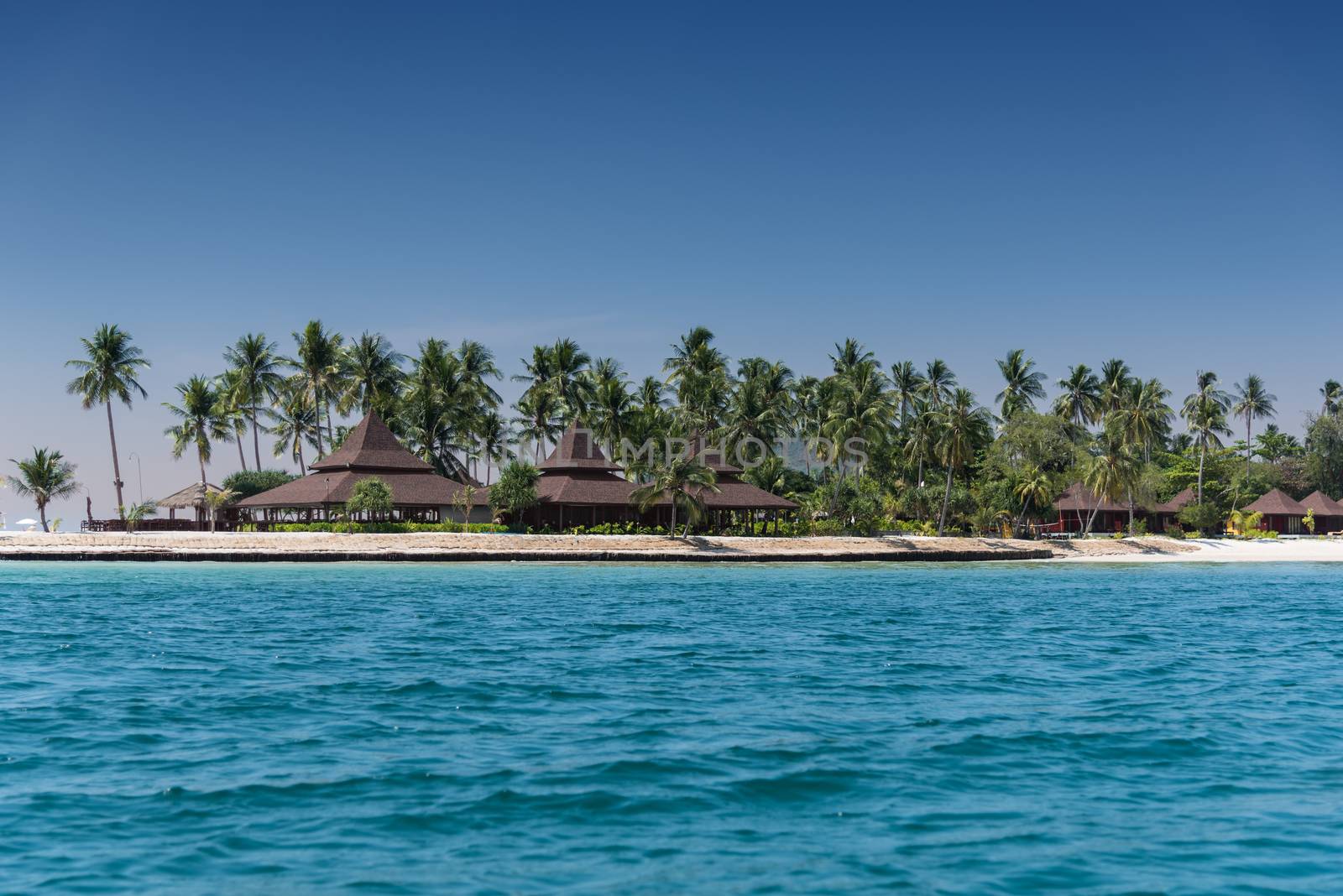 Over water bungalows on island beach with palm trees