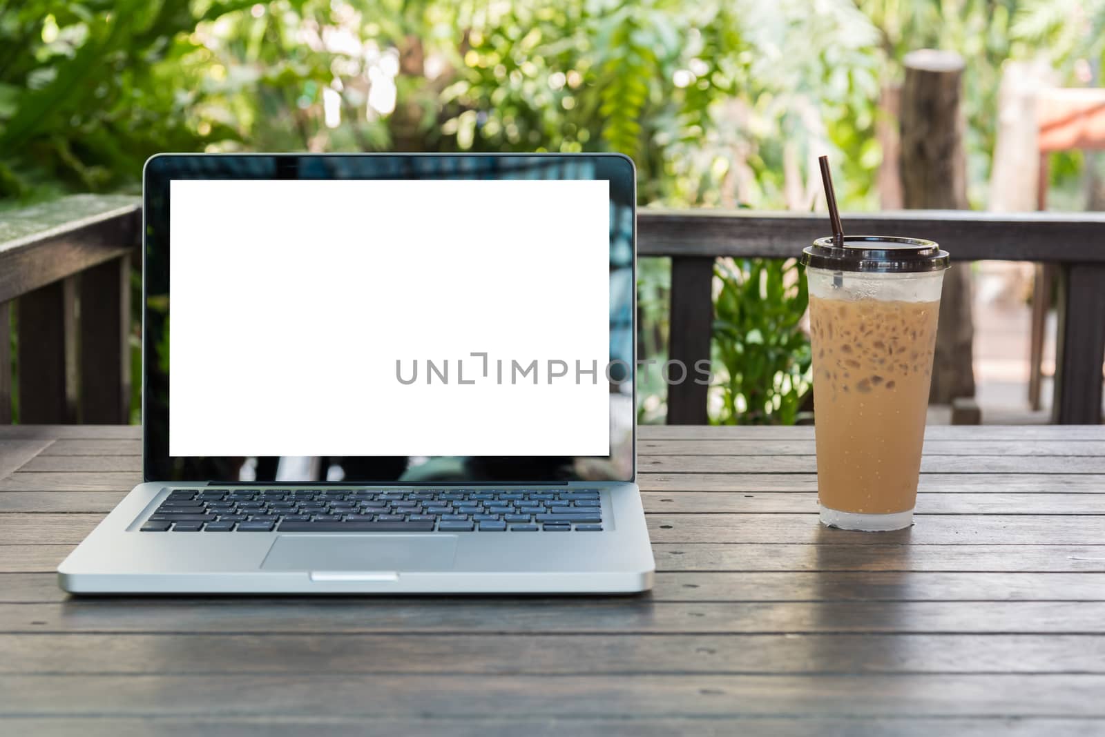 Laptop Notebook with iced coffee cup on wooden table in coffee shop and garden background