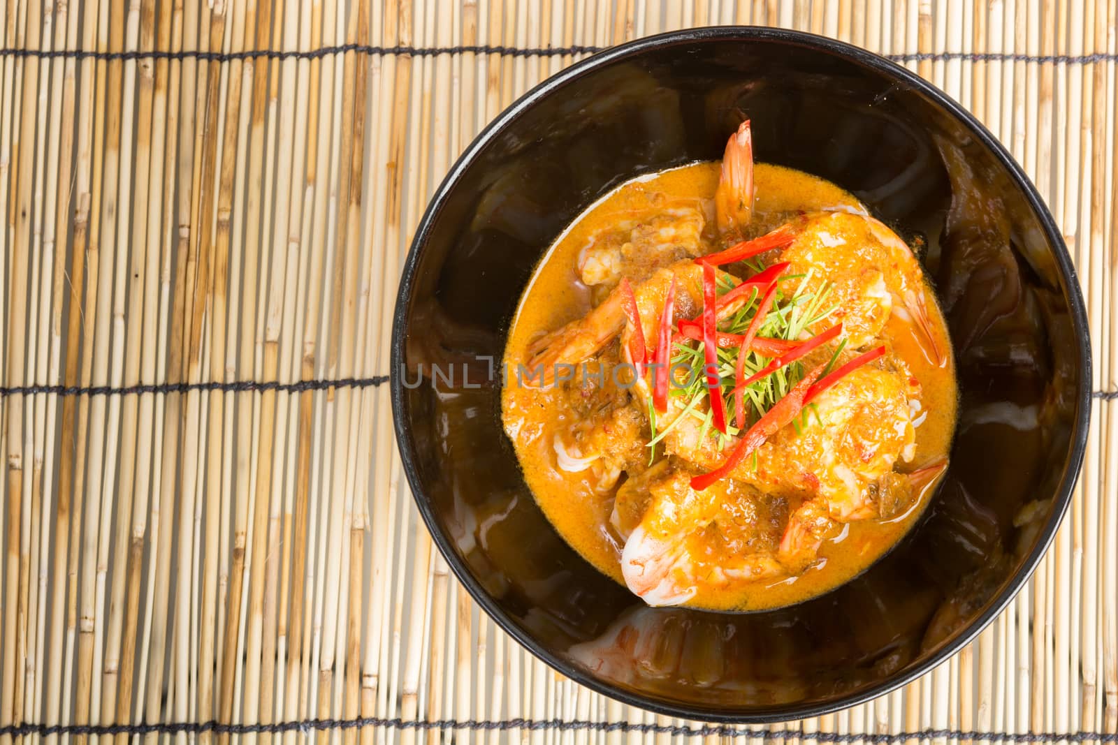 Curry fried shrimps in black cup closeup on table with wooden background